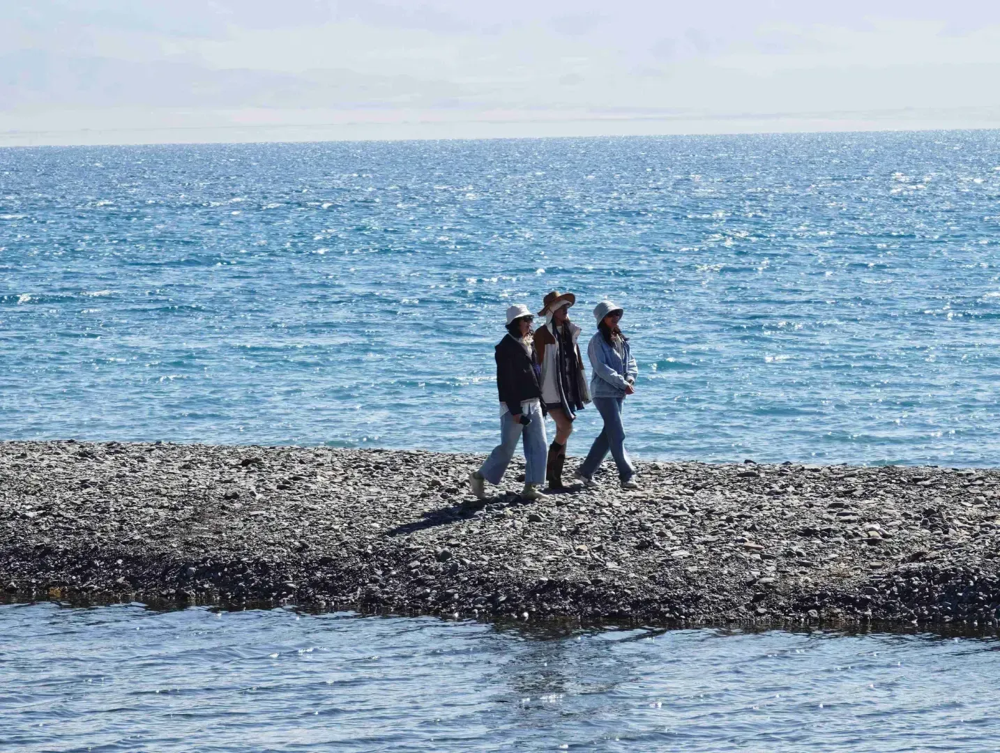 Sayram Lake pebble shore with travelers facing blue water, Xinjiang