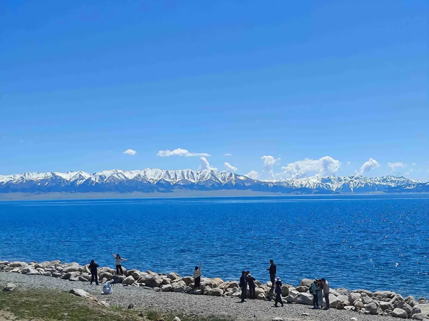 Sayram Lake open shoreline with snowy mountains and visitors in summer, Xinjiang